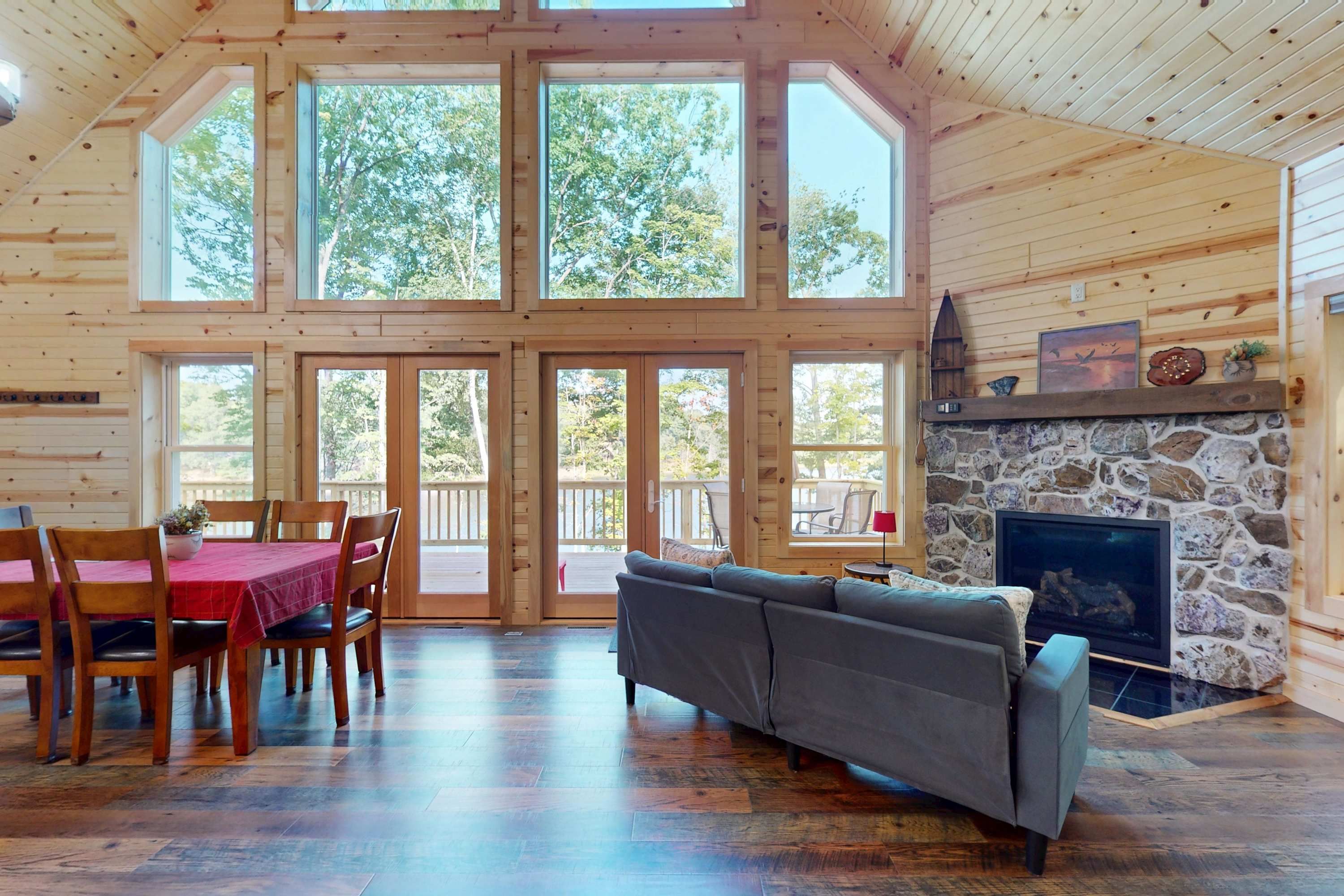 Un interior de cabaña espacioso con comedor, sofá, chimenea y ventanas amplias.