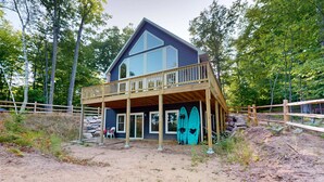 A two-story house with a balcony, surrounded by trees and a wooden fence. - Lakefront Sunrise Lodge: fireplace, deck views, kayaks, pier & firepit (Rhinelander)