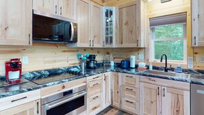 A modern kitchen with wooden cabinetry, stainless steel appliances, and a large window providing natural light. - Lakefront Sunrise Lodge: fireplace, deck views, kayaks, pier & firepit (Rhinelander)