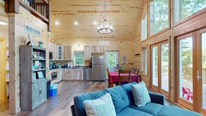 A spacious wooden cabin interior with a kitchen, dining area, and a large window overlooking a deck. - Lakefront Sunrise Lodge: fireplace, deck views, kayaks, pier & firepit (Rhinelander)