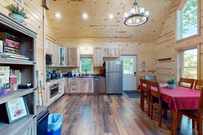 A compact kitchen with wooden cabinets, a stainless steel refrigerator, and a dining area with a red tablecloth.
