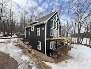 A two-story house with a balcony, surrounded by snow and trees.