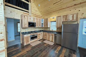 A wooden cabin interior with a kitchen featuring wooden cabinets, a microwave, a refrigerator, and a large window.