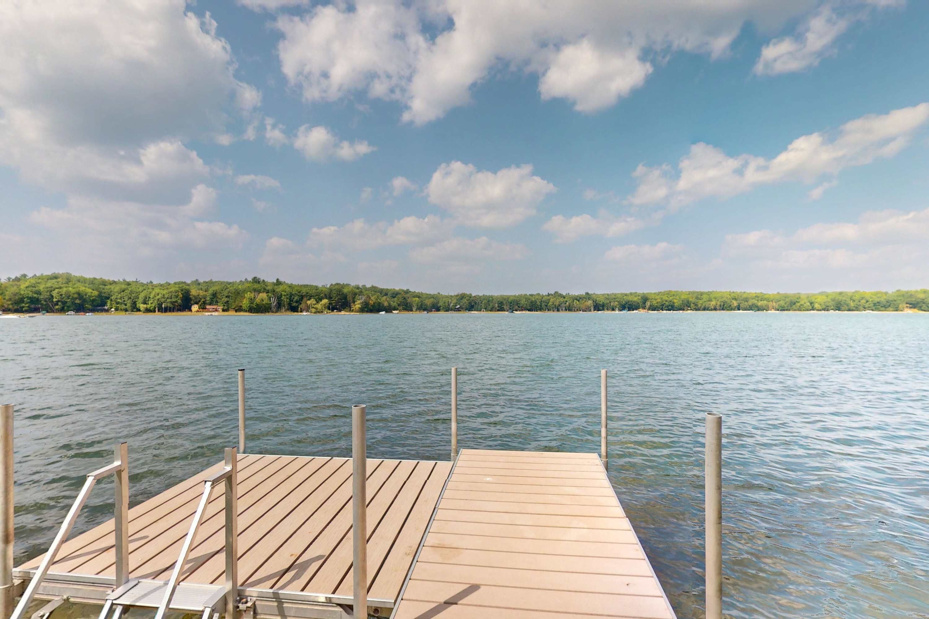 A wooden dock extending into a calm lake with a forested shoreline in the background.