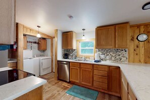A compact kitchen with wooden cabinets, a dishwasher, a washing machine, and a window providing natural light.