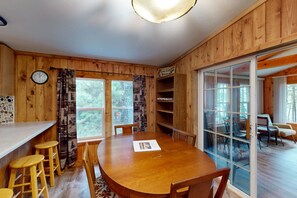 A wooden interior with a dining table, chairs, and a clock on the wall.