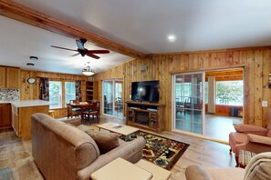 A wooden interior with a television, sofas, a dining table, and a fireplace.