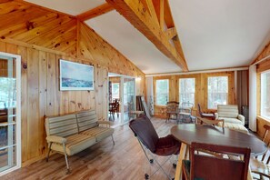 A wooden interior with a dining table, chairs, a sofa, and a painting on the wall.