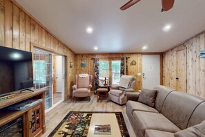 Una sala de estar acogedora con paredes de madera, un televisor de pantalla plana, un sofá, un sillón y una alfombra estampada.