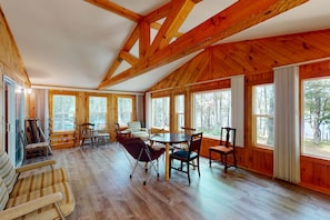 Una habitación amplia con vigas de madera, ventanas grandes y un comedor con sillas y una mesa.