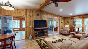 Una habitación con paneles de madera, un ventilador de techo, un televisor, una chimenea y un ventanal grande.
