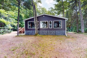 A cabin with a stone foundation, a wooden deck, and a clear view of the surrounding forest.