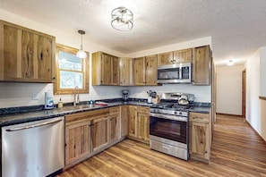 Une cuisine avec des meubles de rangement en bois, un réfrigérateur en acier inoxydable, un four à micro-ondes, une cuisinière et une fenêtre.
