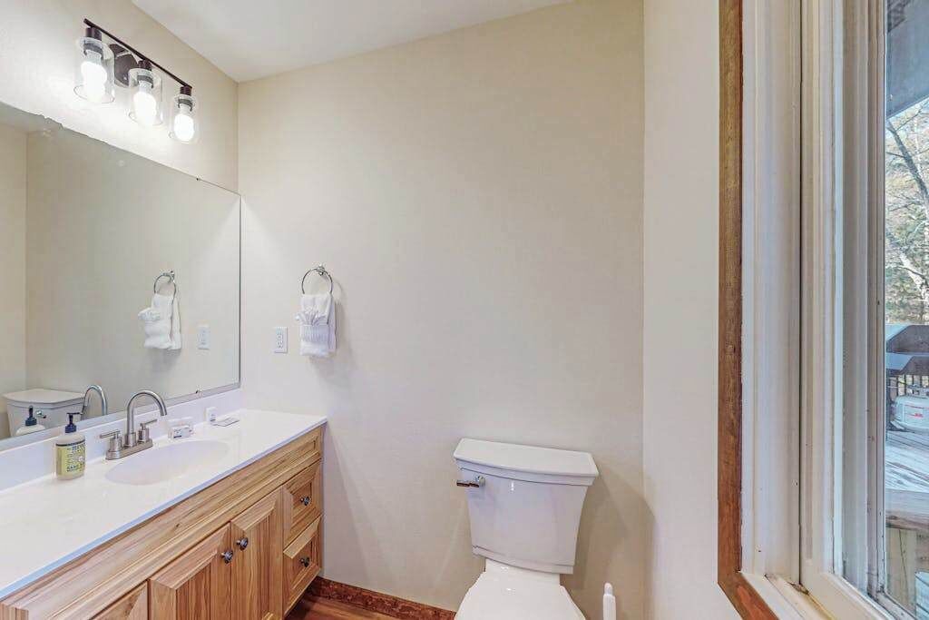 A bathroom with a white sink, wooden vanity, a toilet, and a large mirror.