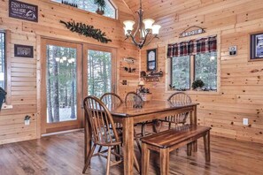 Una cabaña de madera con una mesa de comedor, sillas, una araña y un letrero que dice 'FISH STORIES TOLD HERE'.