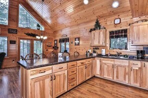 Interior de una cabaña de madera con cocina, comedor y ventanas amplias.