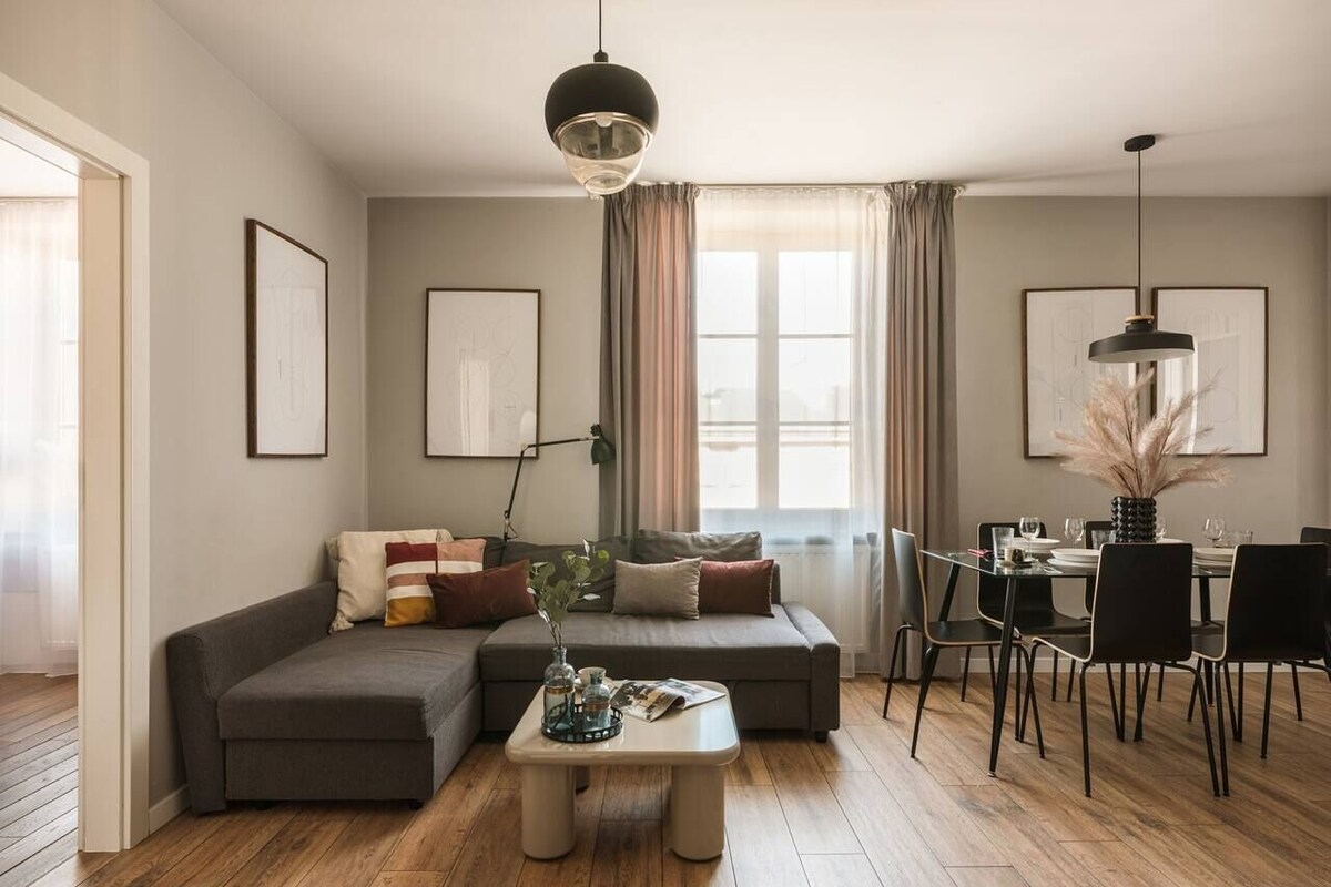 A living room with a sectional sofa, a coffee table, a dining area with chairs, and a window with curtains.