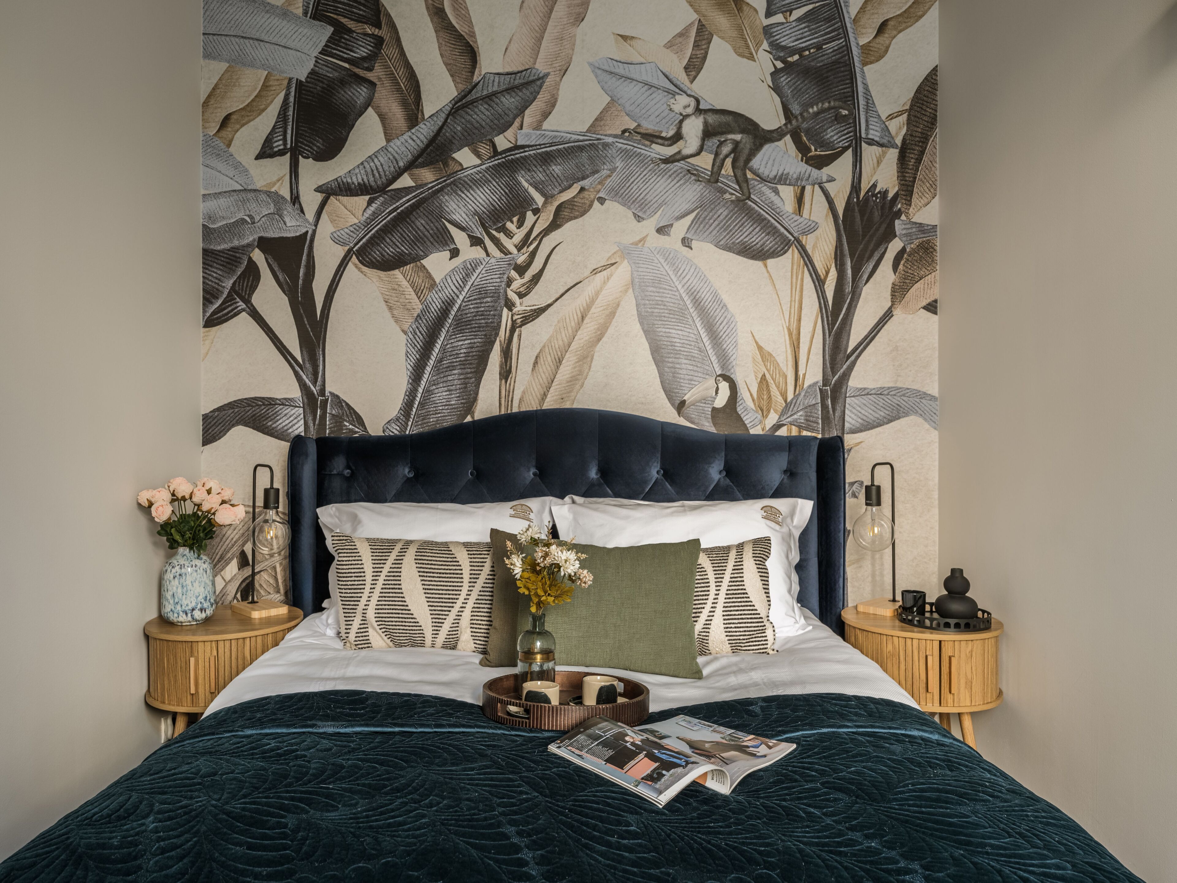 Una cama con cabecera oscura, un tapiz floral en la pared y una revista sobre la cama.