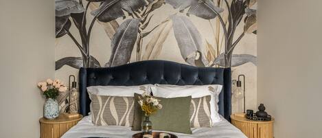 Una cama con cabecera oscura, un tapiz floral en la pared y una revista sobre la cama.