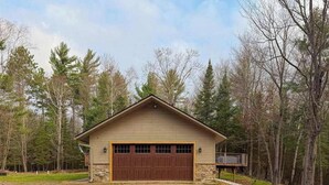 A single-story building with a garage, surrounded by trees. - Cozy Wooded home with WIFI, Gas Grill, Two Kitchens, Near Lakes & Trails (Eagle River)