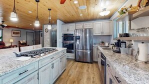 A modern kitchen with granite countertops, stainless steel appliances, and wooden ceiling beams. - Cozy Wooded home with WIFI, Gas Grill, Two Kitchens, Near Lakes & Trails (Eagle River)