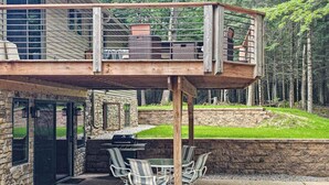 A deck with outdoor furniture, a grill, and a stone wall. - Cozy Wooded home with WIFI, Gas Grill, Two Kitchens, Near Lakes & Trails (Eagle River)