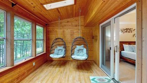 Een kamer met houten wanden, grote ramen, een bed en twee hangstoelen.