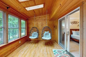 A room with wooden walls, large windows, a bed, and two hanging chairs. - New listing - lakefront home with views, dock, fireplace, foosball, deck, & W/D (Eagle River)