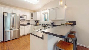 Een moderne keuken met witte kasten, roestvrijstalen apparatuur, een centraal eiland met krukken en hanglampen.