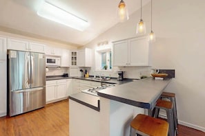A modern kitchen with white cabinets, stainless steel appliances, a central island with stools, and pendant lighting. - New listing - lakefront home with views, dock, fireplace, foosball, deck, & W/D (Eagle River)