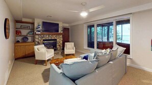 Een woonkamer met een bank, fauteuils, een open haard en een groot raam.