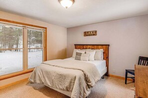 A bedroom with a large window, a bed with a wooden headboard, and a sign on the wall that reads 'LAKE'. - Lakefront, dog-friendly home with dock, kayaks, deck, & washer/dryer (Eagle River)
