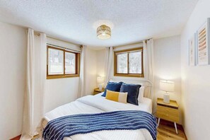 A bedroom with a bed, two bedside tables, a lamp, and a window. - Two Pickerel Lake cabins w/ kayaks, dock, patio, grill & direct access to trails (Eagle River)