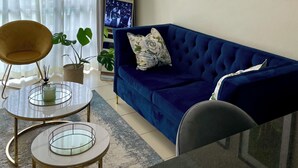 Un salon avec un canapé bleu, une table basse ronde en verre, un fauteuil jaune et un grand miroir.