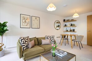 A living room with a sofa, coffee table, and a dining area with chairs and a table. - The Fifth Above Hackney (London)