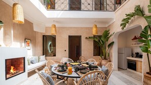 A dining area with a round table, wicker chairs, a fireplace, and a large potted plant. - Dar Shihab exclusive - breakfast included - swimming pool (Marrakech)