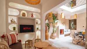 A modern living room with a flat-screen TV, wooden furniture, and a dining area with a high ceiling and natural light. - Dar Shihab exclusive - breakfast included - swimming pool (Marrakech)