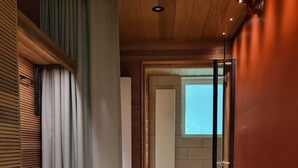 A hallway with a wooden ceiling, a glass door, and a view into a room with a window. - EnjoyNature Resort (Hollola)