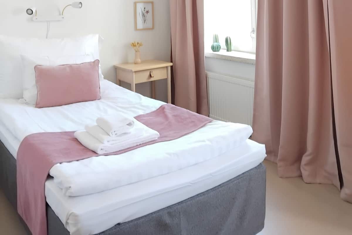 Un dormitorio con cama, mesita de noche, lámpara y ventana con cortinas.