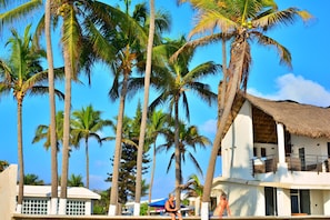 Ein Resort mit Palmen, einem Gebäude mit Reetdach und einem Poolbereich.