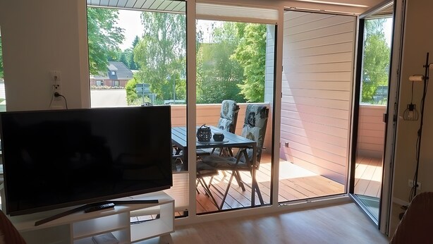 Habitación con televisor sobre un mueble, puerta corrediza de vidrio que da a un patio exterior con mesa y sillas.