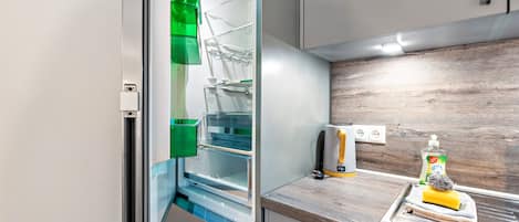 Una cocina moderna con un refrigerador empotrado, un hervidor y una botella de detergente para platos sobre la encimera.