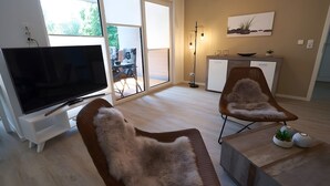 Una sala de estar con televisor, sofá, sillón, mesa de centro y vistas a través de un ventanal.
