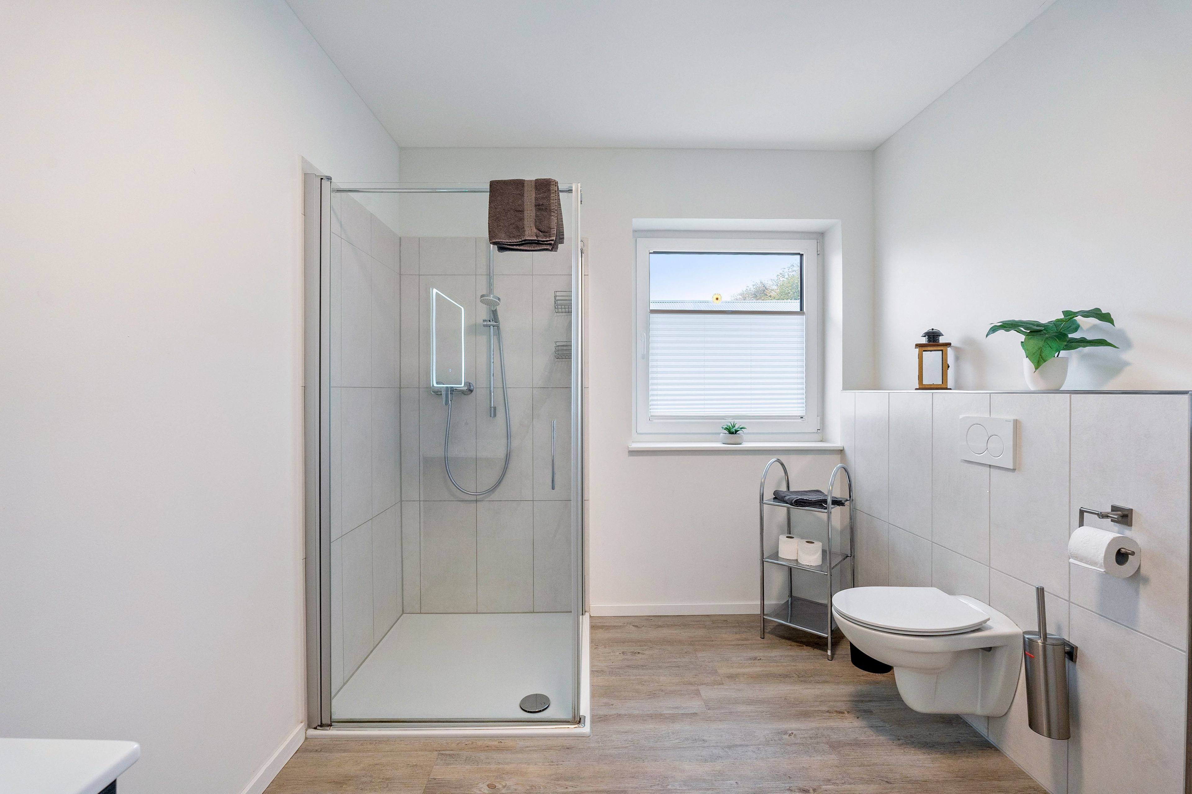 A modern bathroom with a glass-enclosed shower, a toilet, and a window.