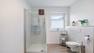A modern bathroom with a glass-enclosed shower, a toilet, and a window.
