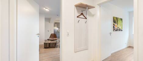 A hallway with a wooden floor, a door with a coat hanger, and a painting on the wall.