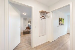 Un pasillo con piso de madera, una puerta con perchero y un cuadro en la pared.