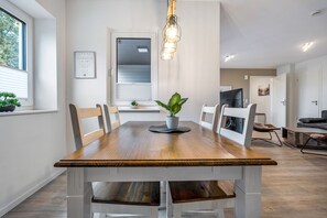 Un comedor con mesa de madera, sillas, una planta en maceta y una lámpara colgante.