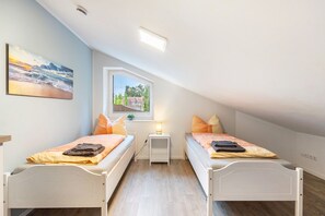 A bedroom with two single beds, a nightstand, a lamp, and a painting of a beach scene.