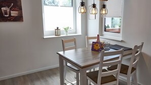 Un comedor con una mesa de madera y sillas blancas, una ventana con vistas, y lámparas colgantes.